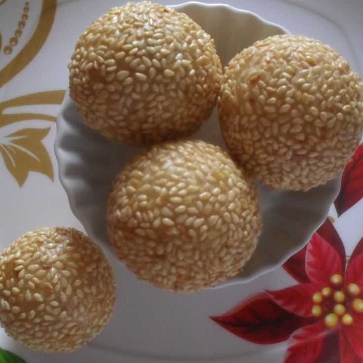 three sesame seed balls on a plate with red and white flowers in the background,