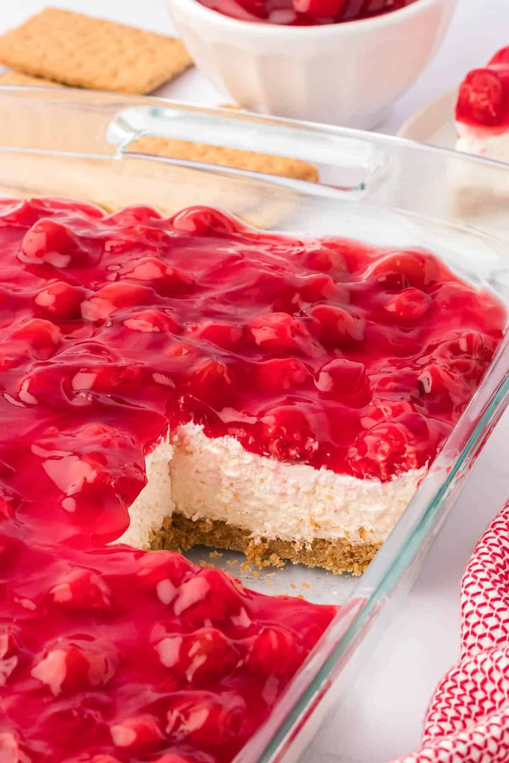 a dessert with cherries on top in a glass dish next to crackers and a bowl of strawberries