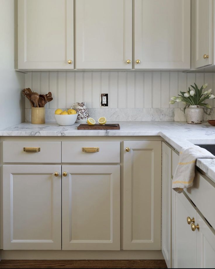 a kitchen with white cabinets and marble counter tops, along with gold pulls on the cabinet doors