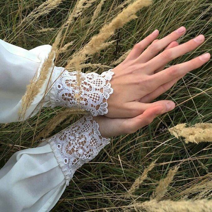 a woman's hand with lace on it is in the middle of some tall grass