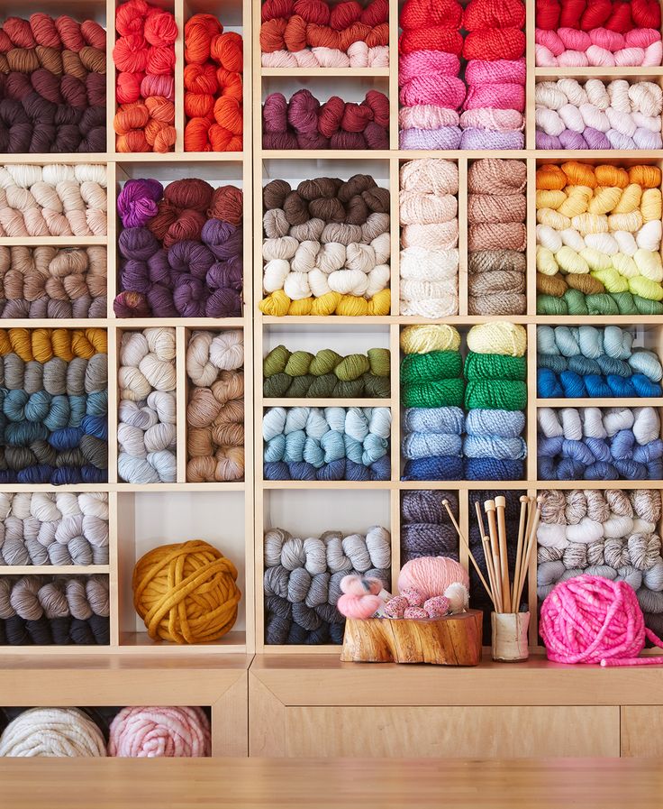 many skeins of yarn are on display in a wooden shelf with knitting needles