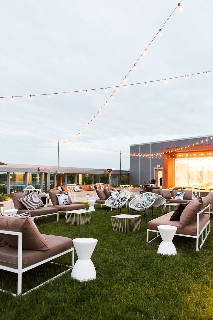 lounge chairs and tables are set up in the grass at an outdoor event with string lights