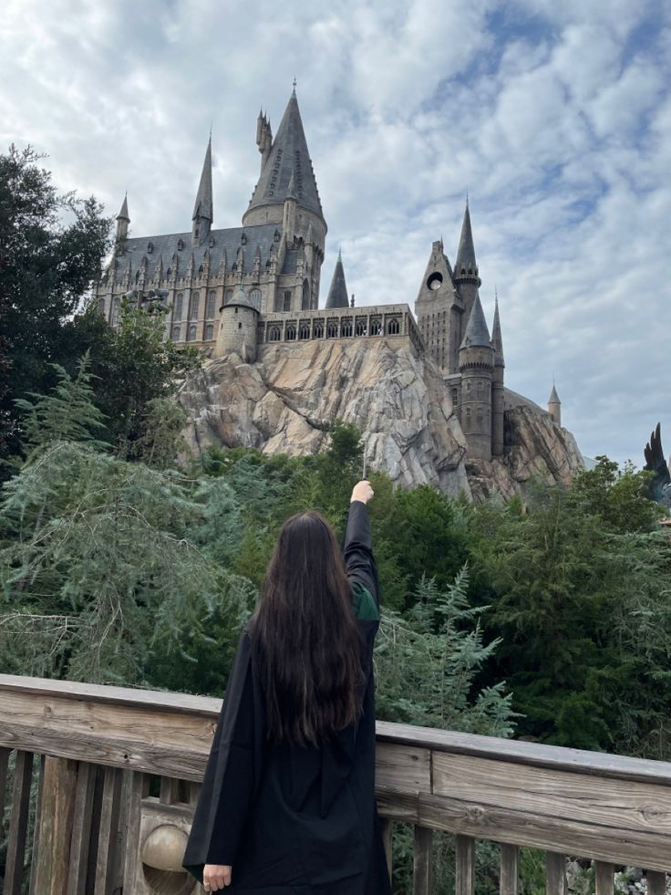 a woman is standing on a bridge looking at hogwarts castle in the distance