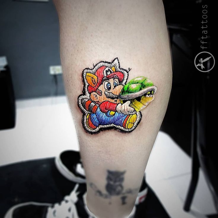 a person with a tattoo on their leg holding a nintendo wii game character sticker