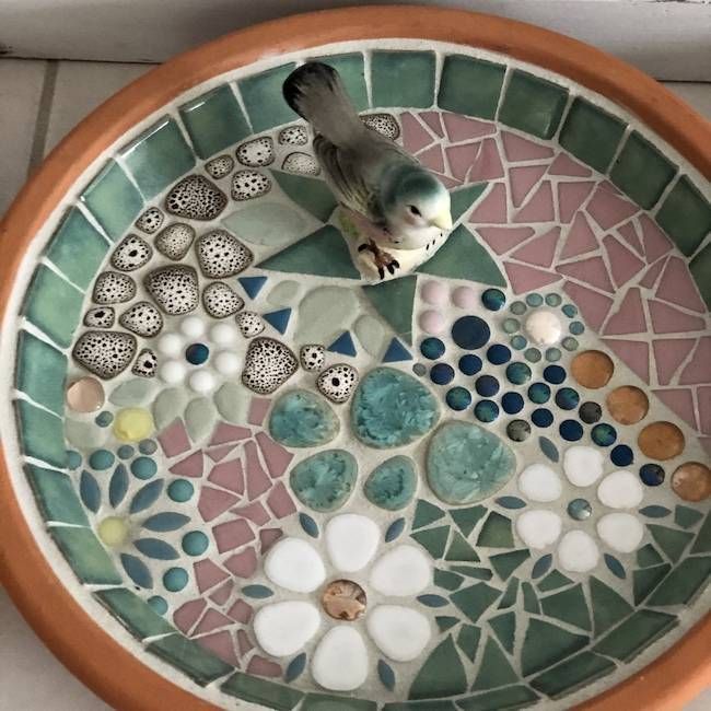 a bird is perched on top of a mosaic bowl that has been decorated with stones and pebbles