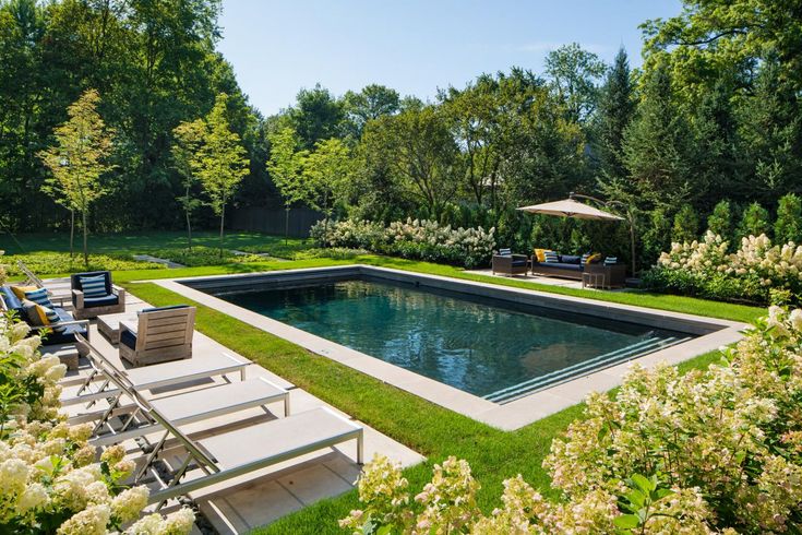 an outdoor swimming pool surrounded by greenery and lawn chairs with umbrellas on the side