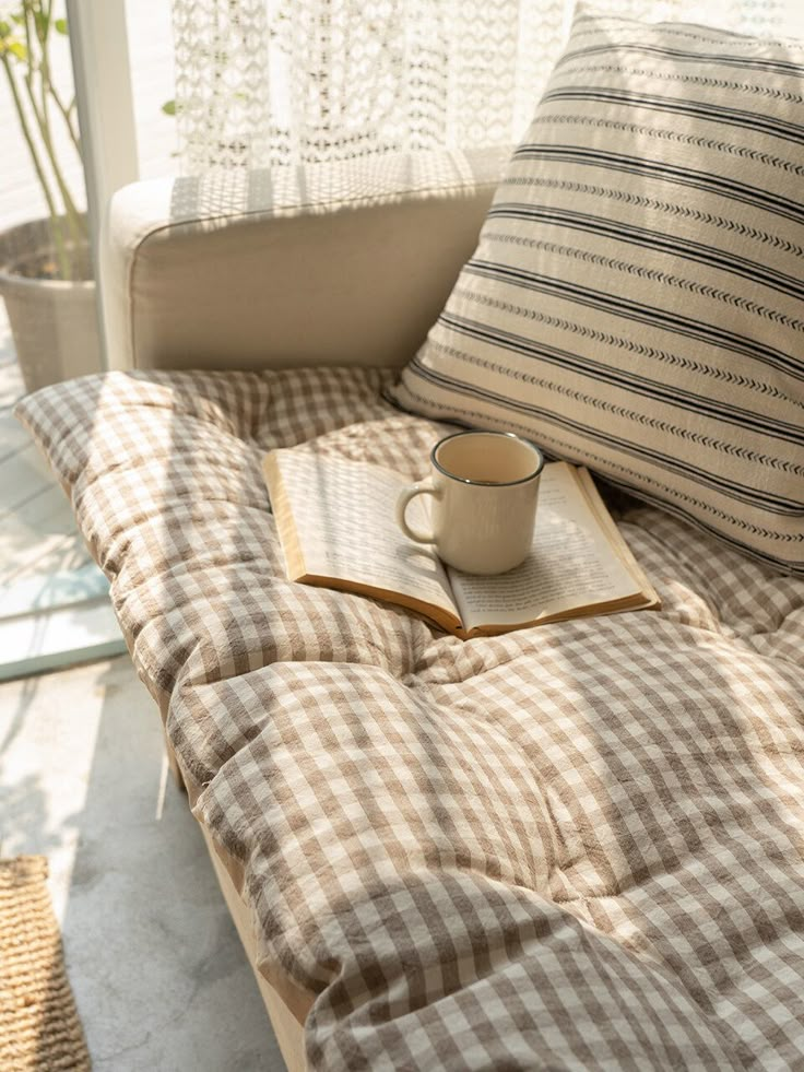 a coffee cup and book sitting on top of a couch in front of a window