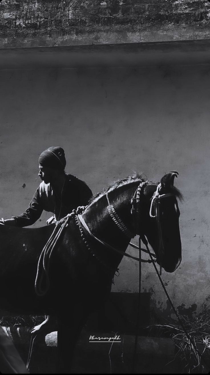 a black and white photo of a man sitting on a horse next to a wall