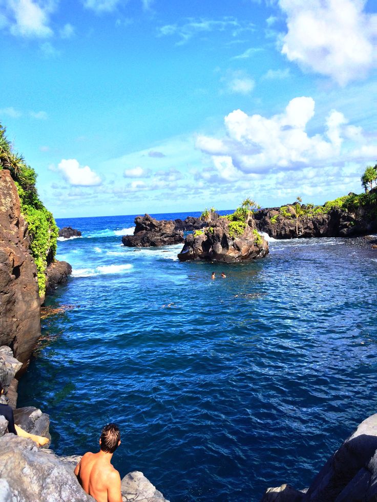 a man sitting on the edge of a cliff looking out at the ocean and rocks