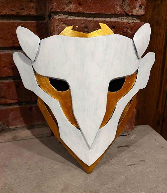 a white mask with gold accents on top of a wooden table next to a brick wall