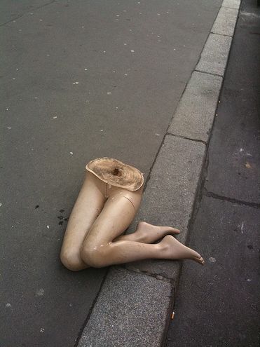 a mannequin laying on the sidewalk next to a pole with a piece of cloth covering it's body