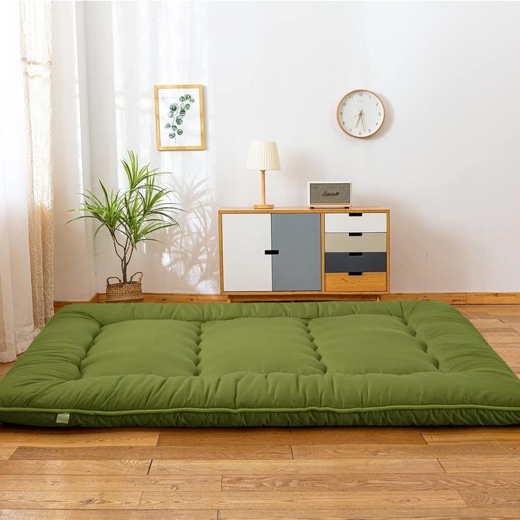 a green mattress on the floor in front of a white wall with a clock above it