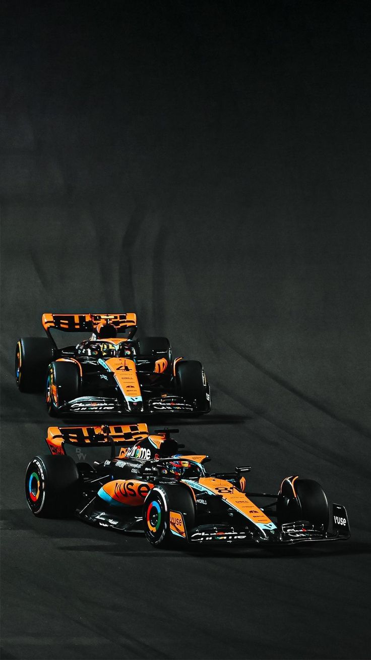 three racing cars driving on a track in the night time, one is orange and white