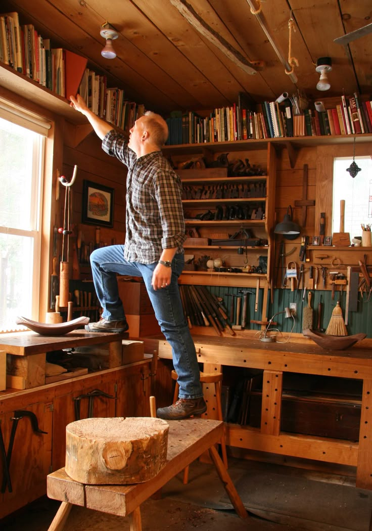 a man standing on a wooden bench in a room filled with woodworking tools and books