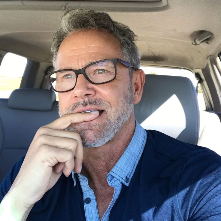 a man wearing glasses sitting in the back seat of a car with his hand on his chin