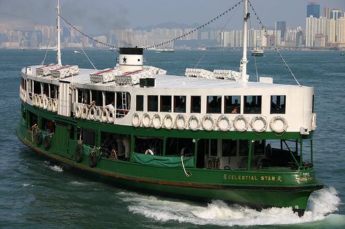 a green and white boat traveling on the water with buildings in the backgroud