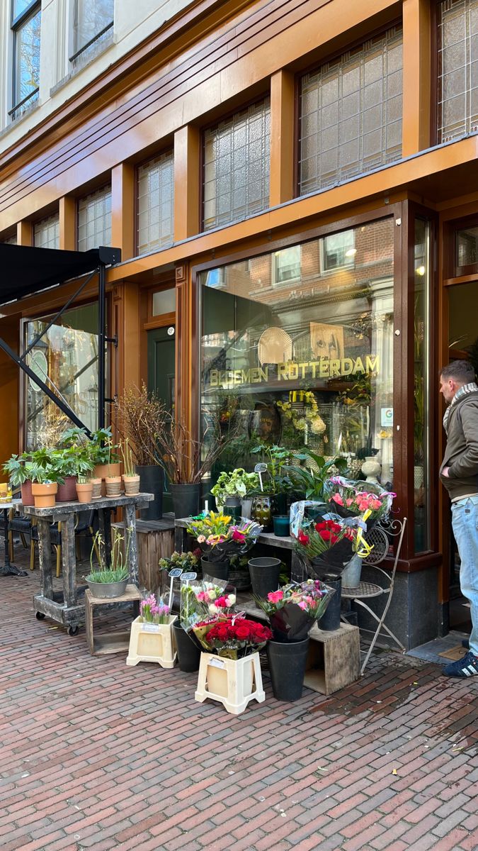 a man standing in front of a flower shop with lots of flowers on the sidewalk