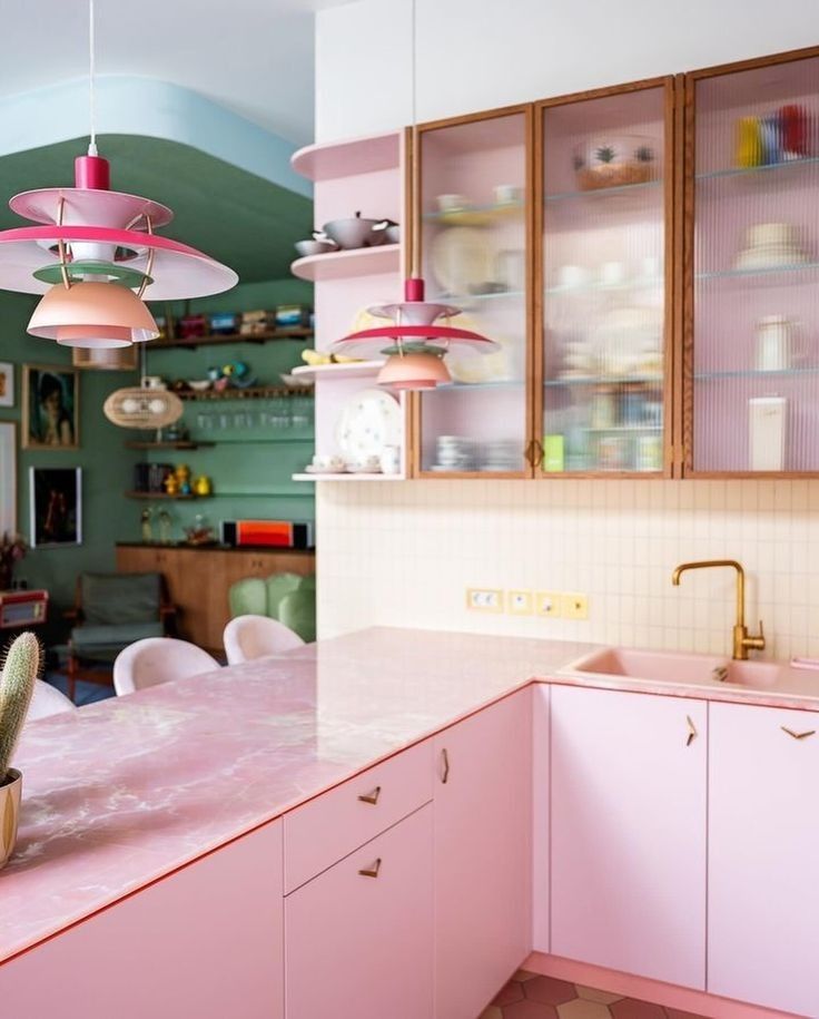 a kitchen with pink counter tops and hanging lights above the sink, in front of a dining room table