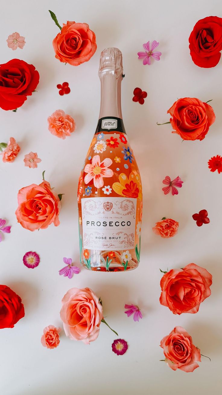 a bottle of rose wine surrounded by pink and red flowers on a white surface with petals