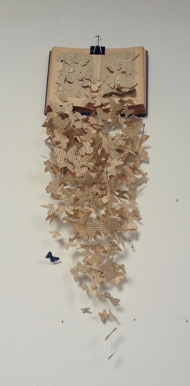 an open book with many pieces of paper cut into the shape of butterflies hanging from it