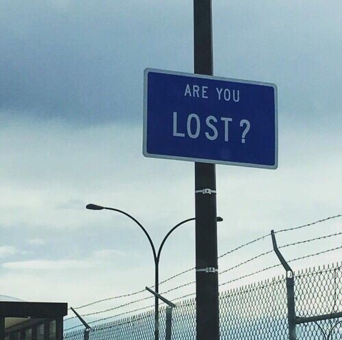 a blue sign that says are you lost? on a pole next to a fence