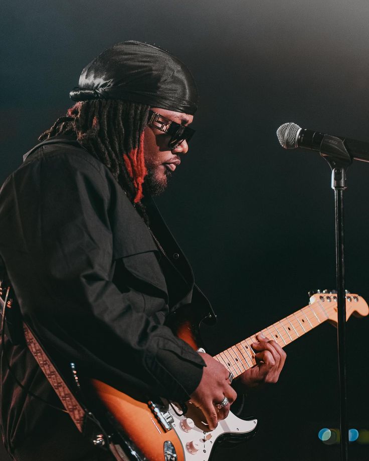 a man with dreadlocks playing an electric guitar in front of a microphone on stage