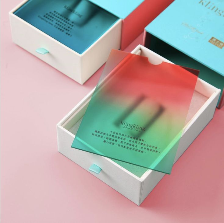 three boxes that are open on a pink surface with blue and green paper in them