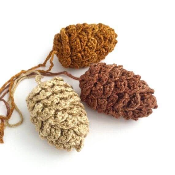 three crocheted pinecones are shown on a white surface, one is brown and the other is tan