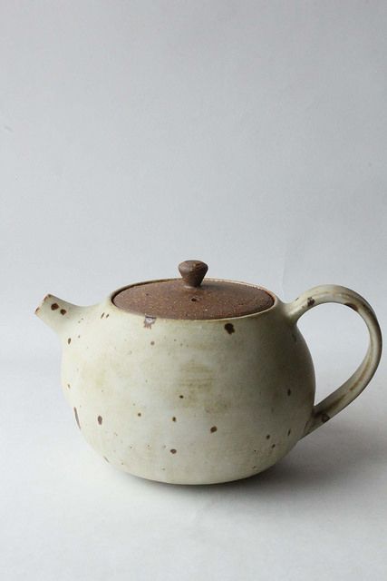 a white teapot with brown speckles sits on a plain surface, ready to be used as a saucer