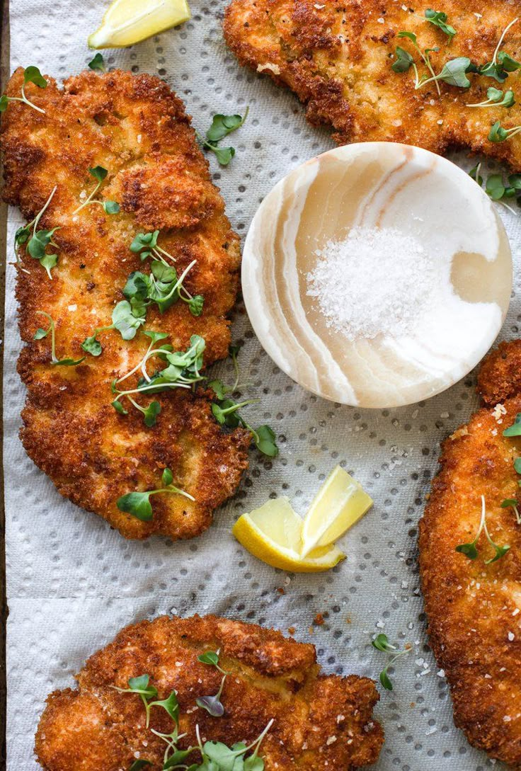 fried fish with lemon and parsley on a sheet of paper next to a spoon