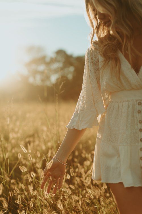 a woman in a white dress is walking through tall grass with her hand on the ground