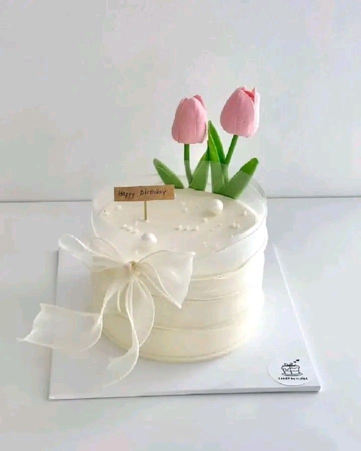 a white cake with pink tulips on top and a card attached to it