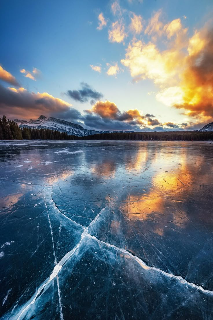 the sun is setting over an icy lake