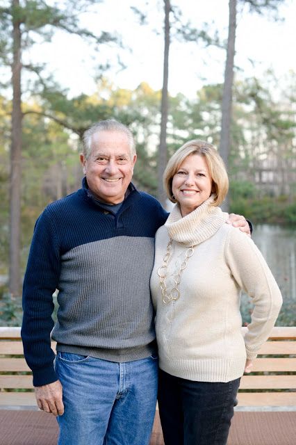 an older man and woman standing next to each other on a bench in front of trees