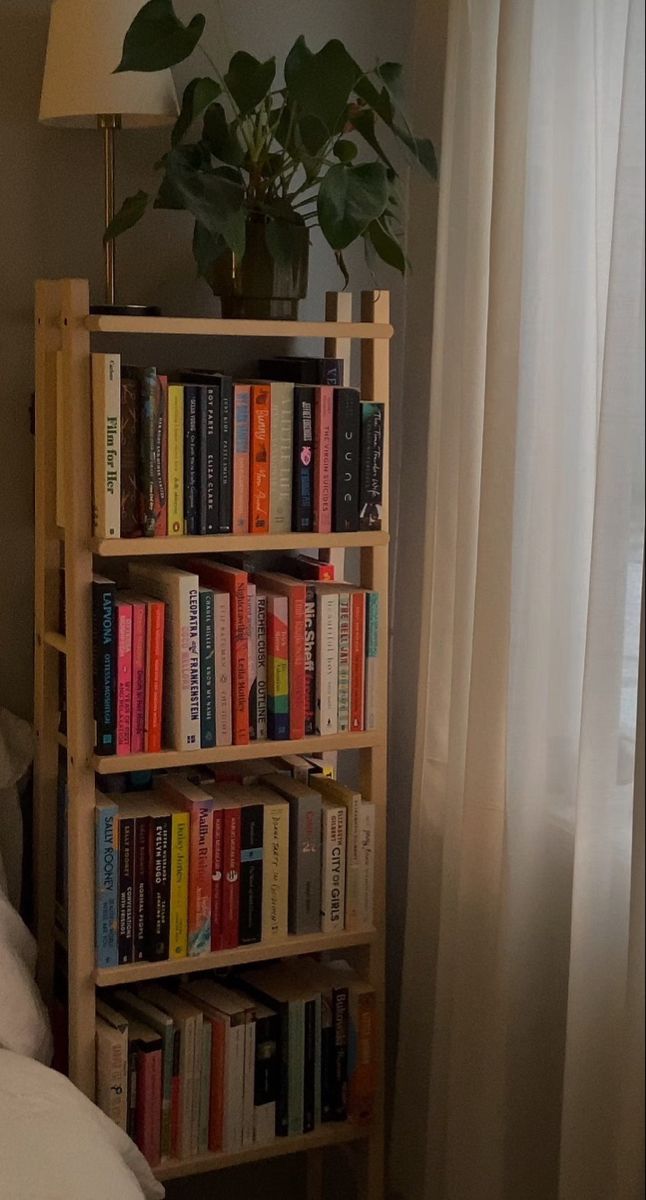 a bookshelf filled with lots of books next to a lamp on a bed