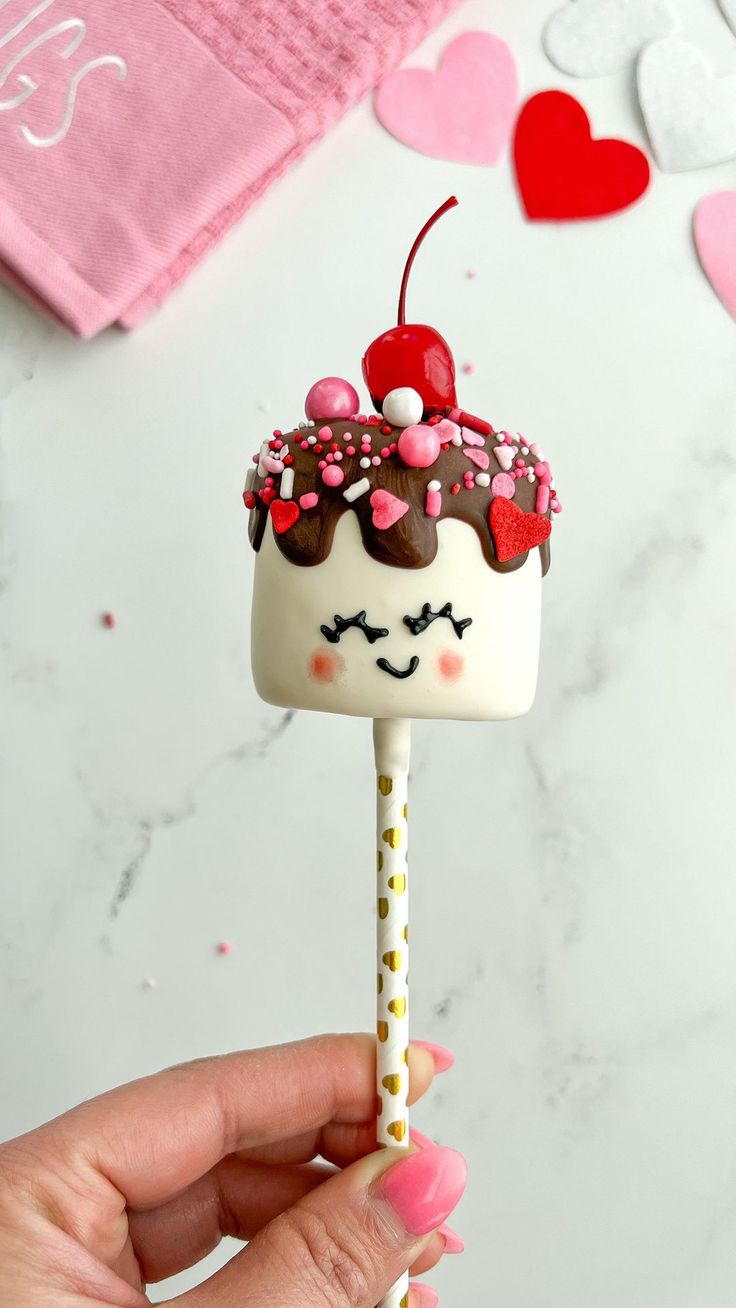 a hand holding a cake pops with chocolate frosting and sprinkles on top