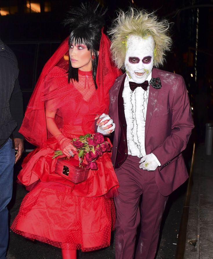 a man and woman dressed up in costumes walking down the street with one holding flowers