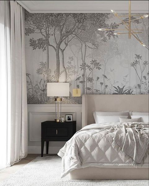 a white bed sitting under a chandelier next to a wall with trees on it