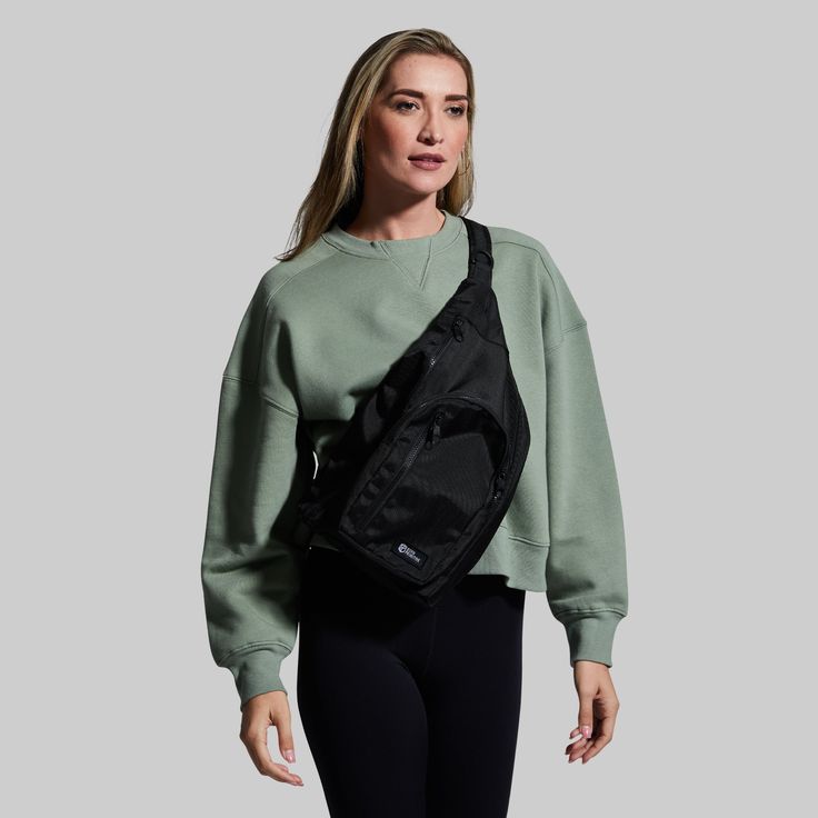 a woman wearing a green sweatshirt and black leggings is holding a black fanny bag