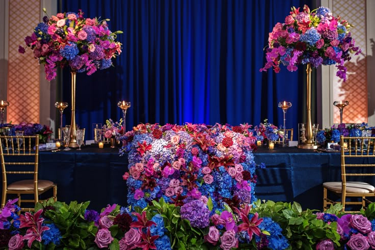 purple and blue flowers are on display at a banquet table with tall centerpieces