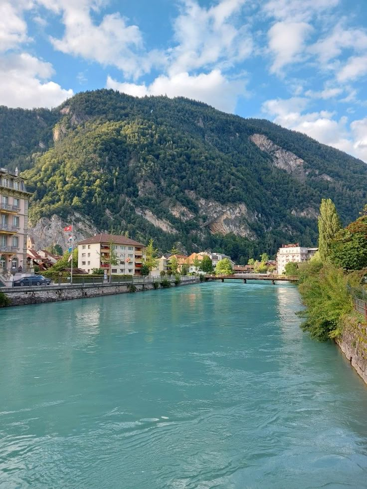 a river running through a lush green hillside next to a town under a blue sky