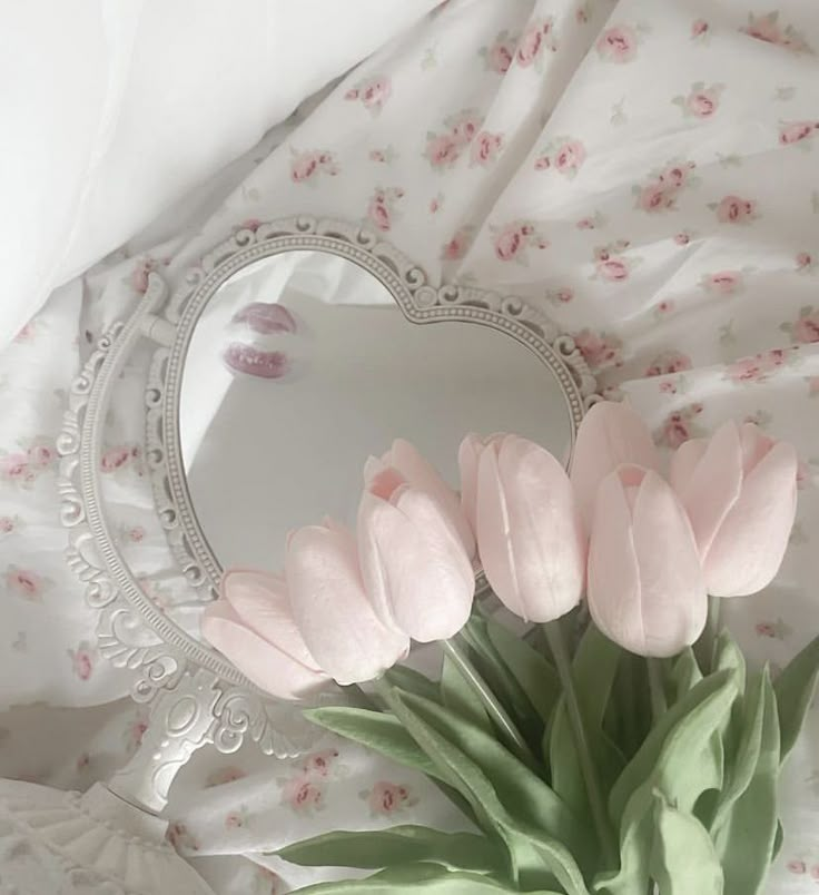 a bouquet of pink tulips sitting on top of a bed next to a heart shaped mirror