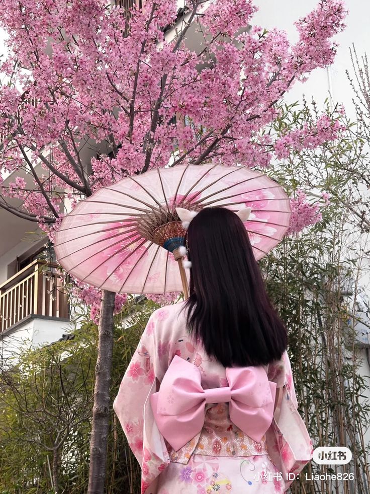 a woman wearing a pink kimono and holding an umbrella in front of cherry blossom trees