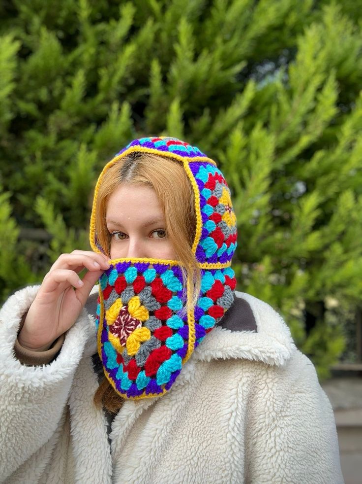 a woman in a white coat is holding up a colorful piece of cloth to her face