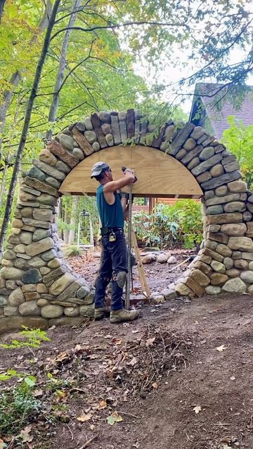 a man standing in front of a stone arch made out of rocks and wood with a hammer