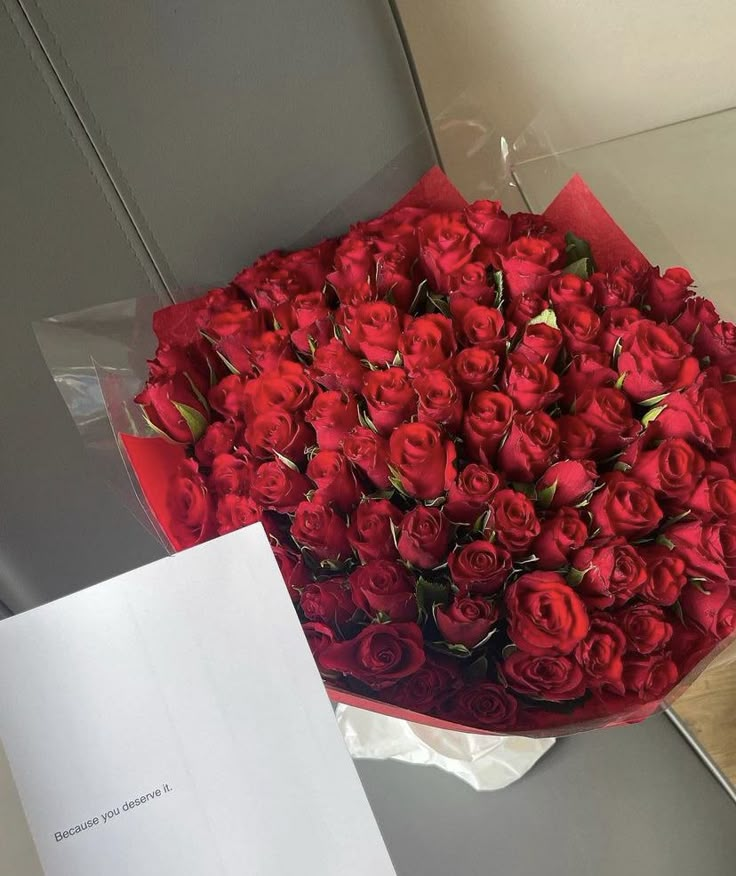 a bouquet of red roses sitting on top of a table next to a piece of paper