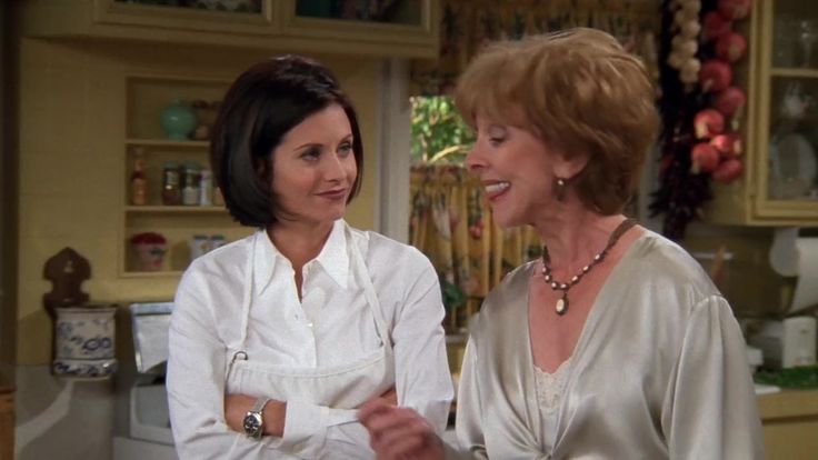 two women standing in a kitchen talking to each other and smiling at one another's side