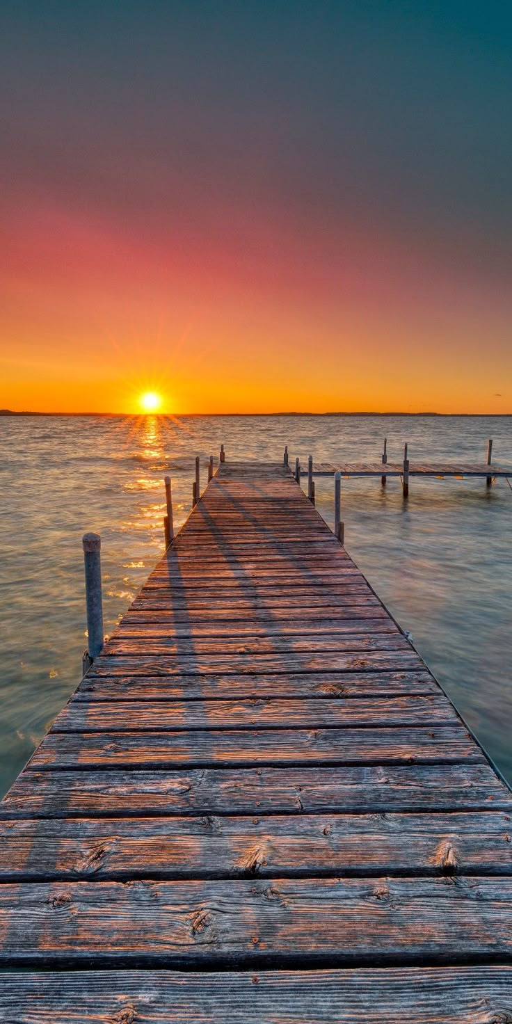 the sun is setting at the end of a pier in the ocean with no people on it