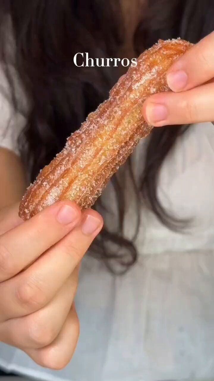 a woman holding a sugar covered donut in her hands with the words churro on it