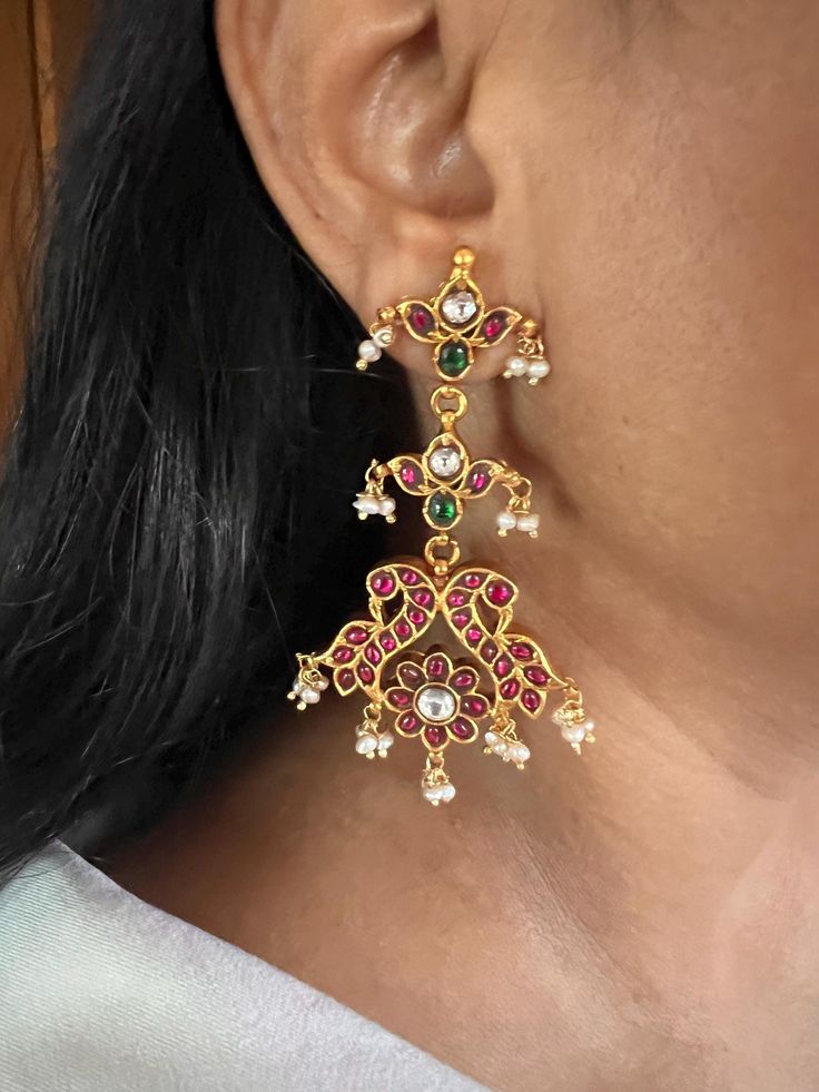 These stunning Kempu 925 silver earrings are meticulously handcrafted by fine jewelry artisans, featuring an elegant peacock design with natural freshwater pearl drops. Perfect for destination weddings and festive seasons like Navratras, these earrings combine traditional charm with intricate detailing, making them an ideal accessory for special occasions. Weight: 36 grams per pair Materials: 925 Silver, Kempu Stones, Freshwater Pearls, Gold Plated. Closure Type: Push Back Closure. Dimensions: Length is 7.5 cm and width is 4 cm. Designed to enhance your festive look, these earrings offer a perfect blend of comfort and sophistication. Elegant Peacock Design Dangle Earrings, Elegant Dangle Earrings With Peacock Design, Elegant Sterling Silver Earrings With Peacock Design, Elegant Earrings With Peacock Design For Gift, Elegant Peacock Design Earrings As Gift, Elegant Sterling Silver Bridal Earrings For Festive Season, Elegant Sterling Silver Bridal Earrings, Elegant Festive Sterling Silver Bridal Earrings, Elegant Silver Earrings With Peacock Design